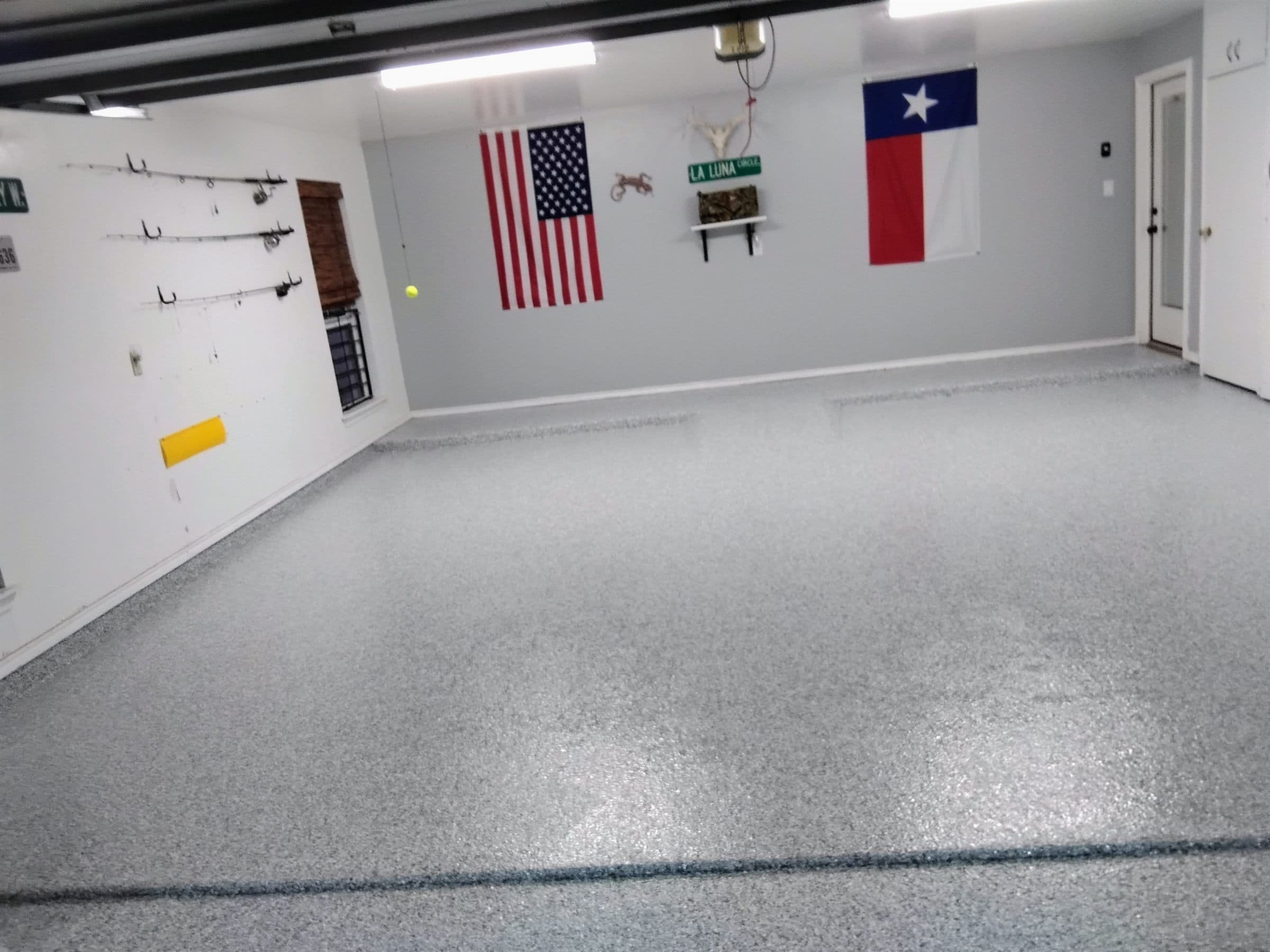 Grey and blue flake epoxy floor in a finished residential garage, walls and storage hooks visible behind it.