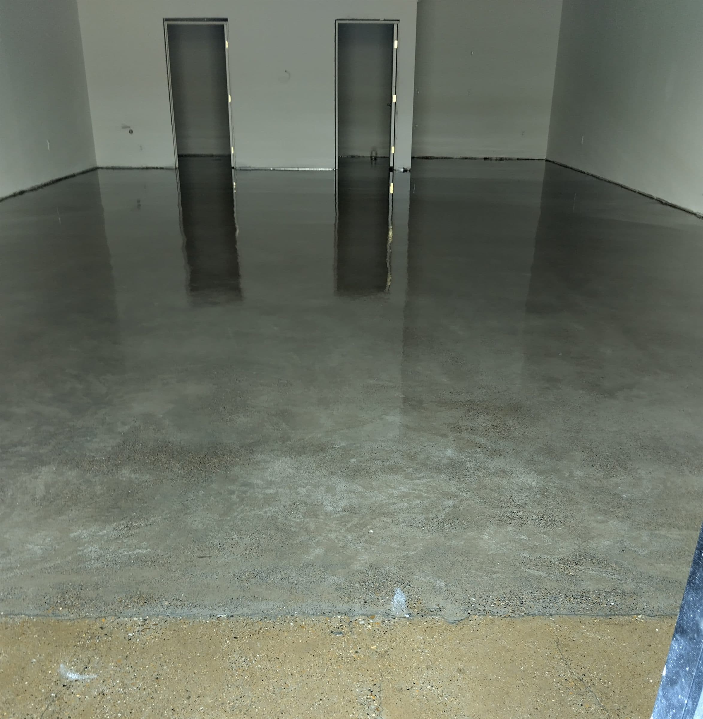 Grey polished concrete floor in an interior room, reflecting the doors on the far wall.