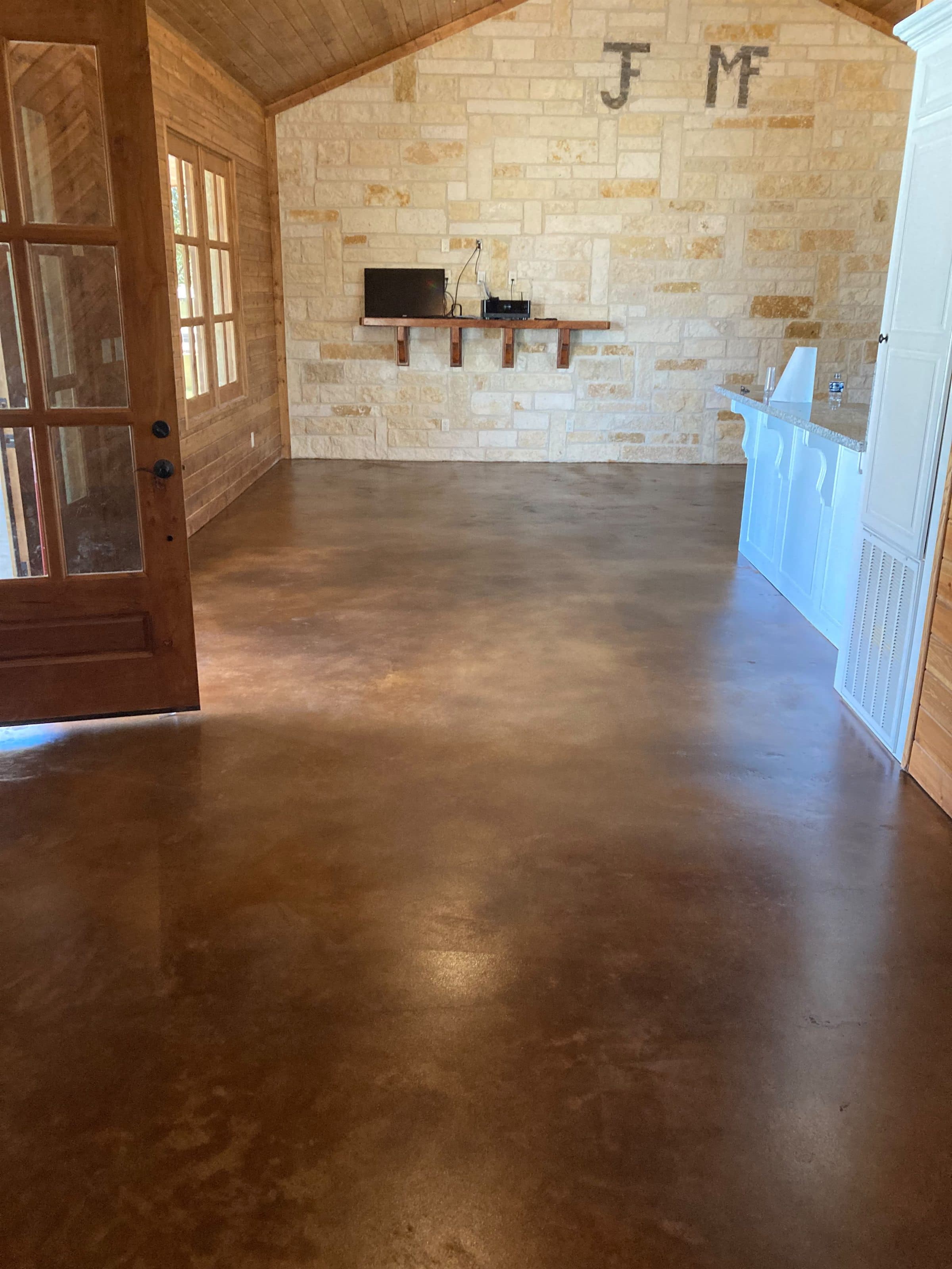 Warm brown stained concrete floor in a residential interior with a stone feature wall.