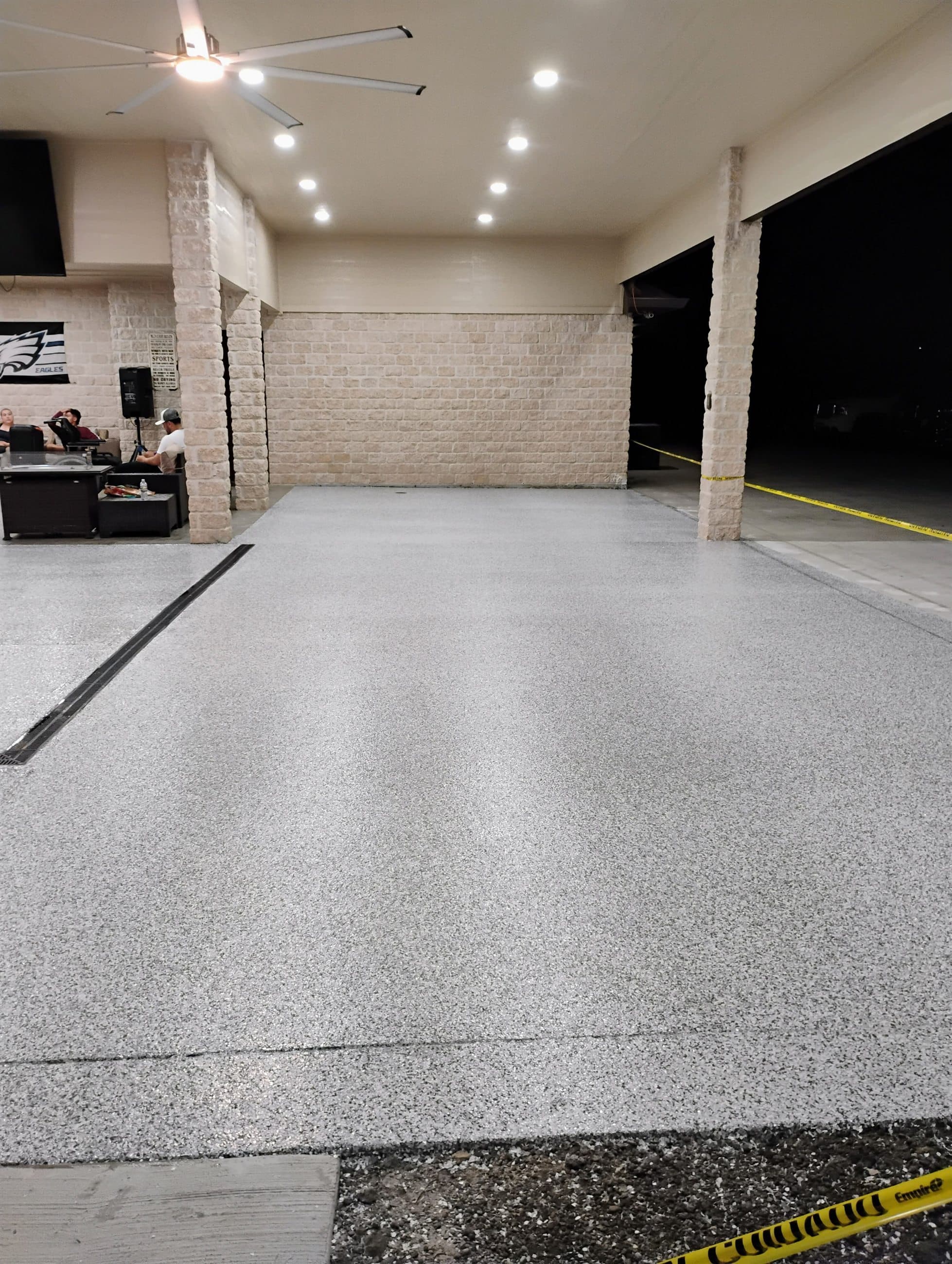 Light grey flake floor under a covered outdoor patio, brick columns framing the open bay.