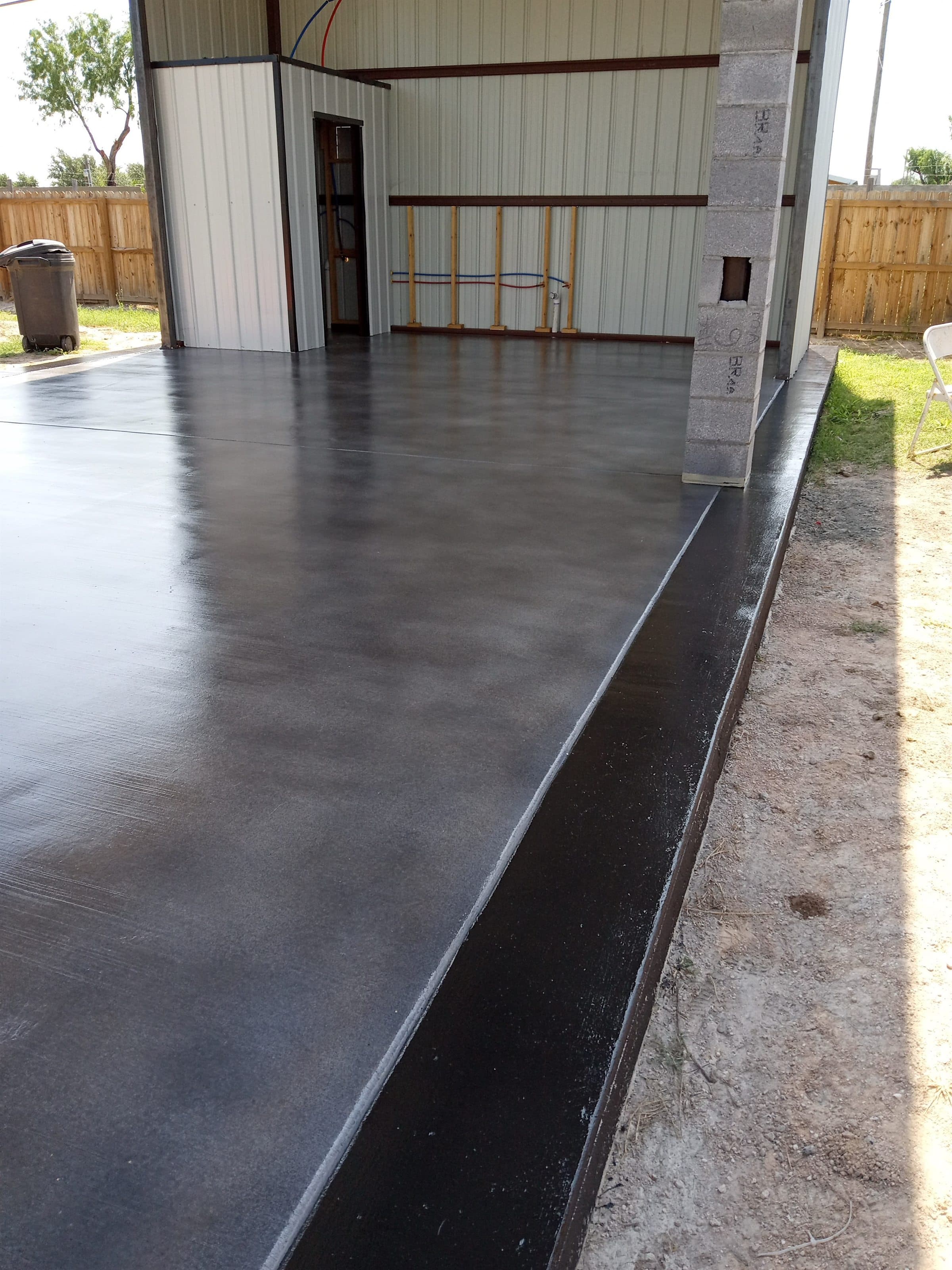 Charcoal stained and sealed exterior concrete slab running alongside a metal building.